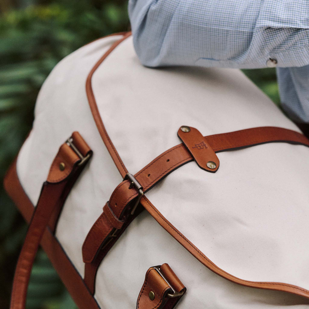 A person carries the Tom Beckbe Perdido Canvas Weekender Duffel Bag, wearing a light blue checkered shirt.