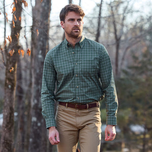 Man in a Tom Beckbe Powell Performance Shirt and khaki pants walks outdoors near trees on a clear day.