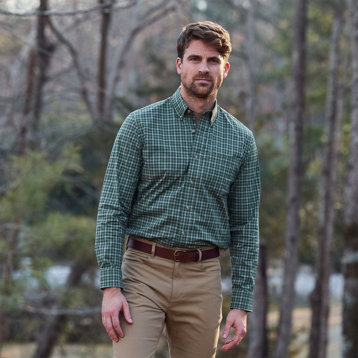 Man in Tom Beckbe Powell Performance Shirt (UPF 30+) and khaki pants stands outdoors in a wooded area.