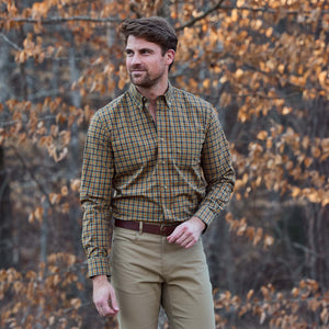 A man wears the Tom Beckbe Powell Performance Shirt and khaki pants outdoors amid autumn trees with brown leaves.