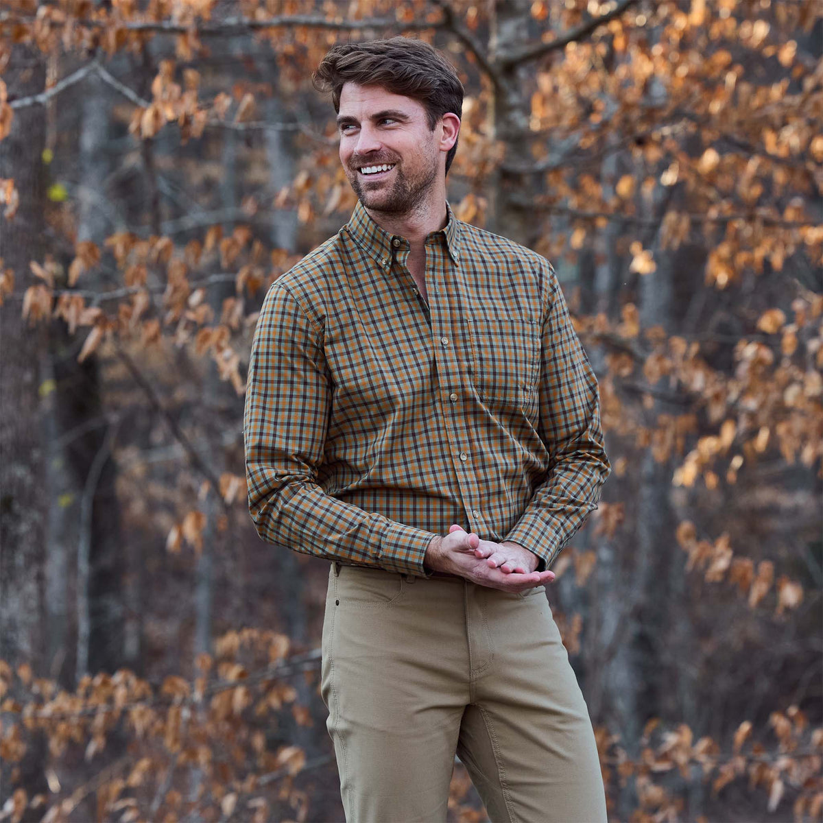 Man outdoors in a Tom Beckbe Powell Performance Shirt and khaki pants, framed by autumn foliage.