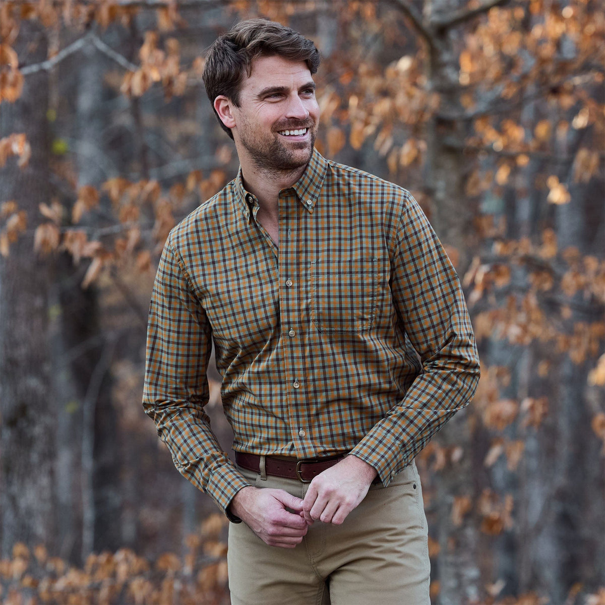 Man wearing the Tom Beckbe Powell Performance Shirt stands outdoors before autumn trees with brown leaves.