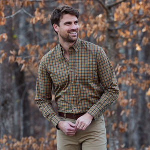 Man wearing the Tom Beckbe Powell Performance Shirt stands outdoors before autumn trees with brown leaves.