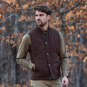 Man in a Tom Beckbe Powell Performance Shirt and brown quilted vest, outdoors with autumn foliage in the background.