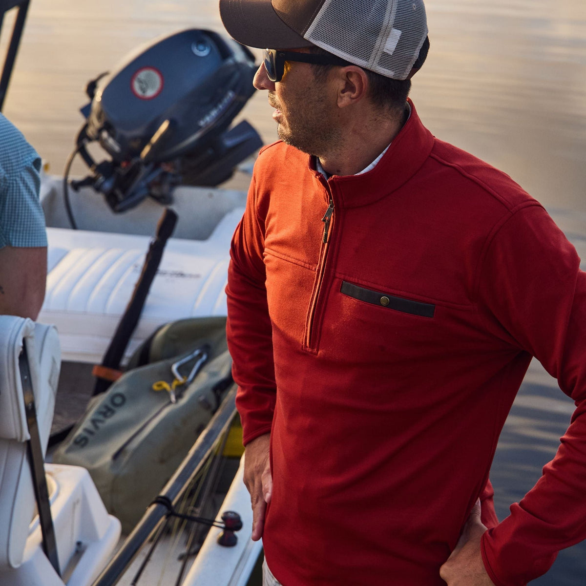 Man in a Tom Beckbe Tucker Fleece Quarter Zip stands on a boat, gazing away near another person and a motor.