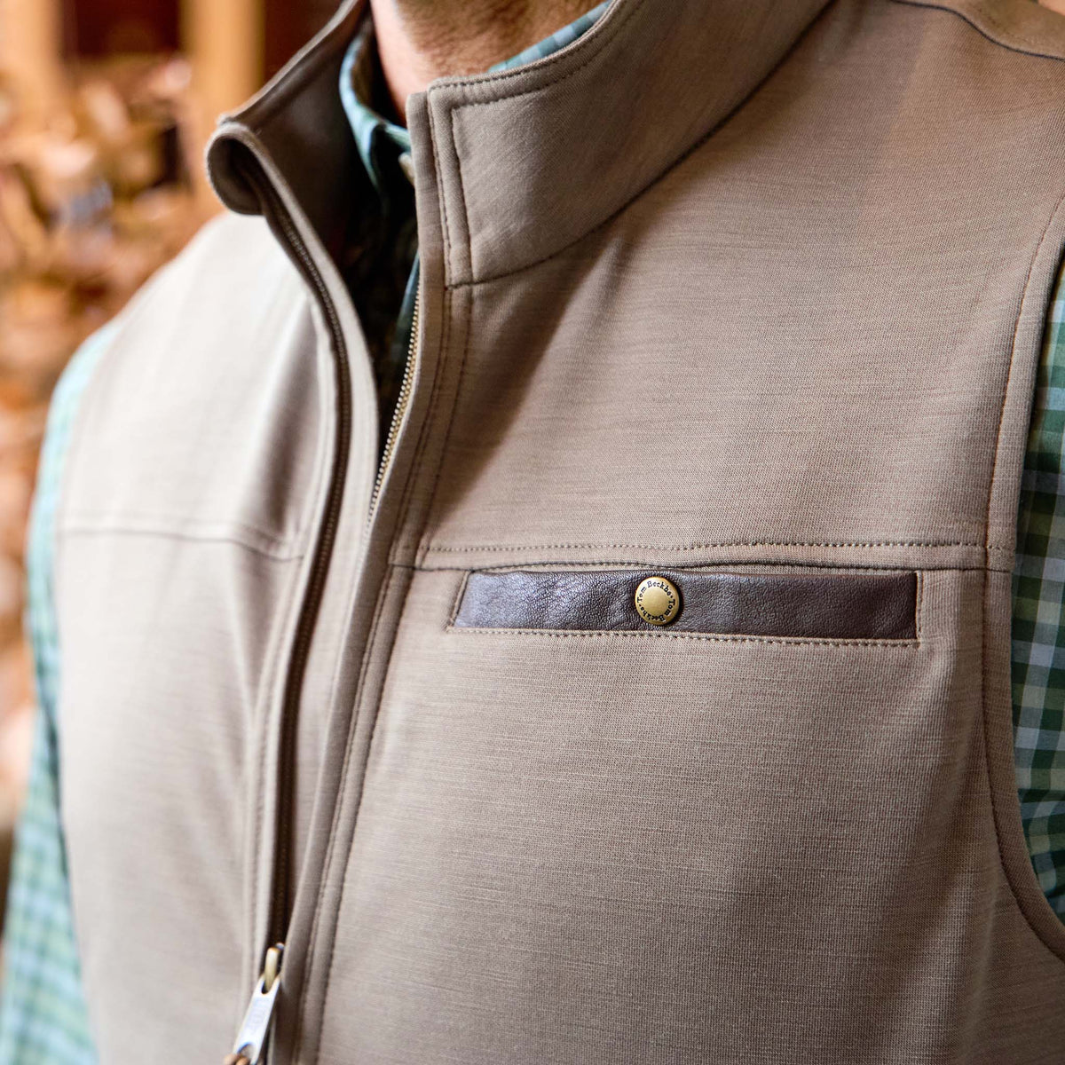 Man wearing a Tom Beckbe Tucker Fleece Vest in tan with snap-button chest pocket over a green plaid shirt.