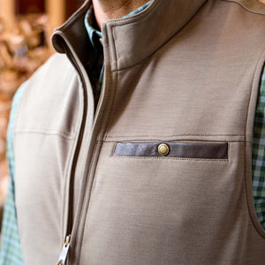 Man wearing a Tom Beckbe Tucker Fleece Vest in tan with snap-button chest pocket over a green plaid shirt.