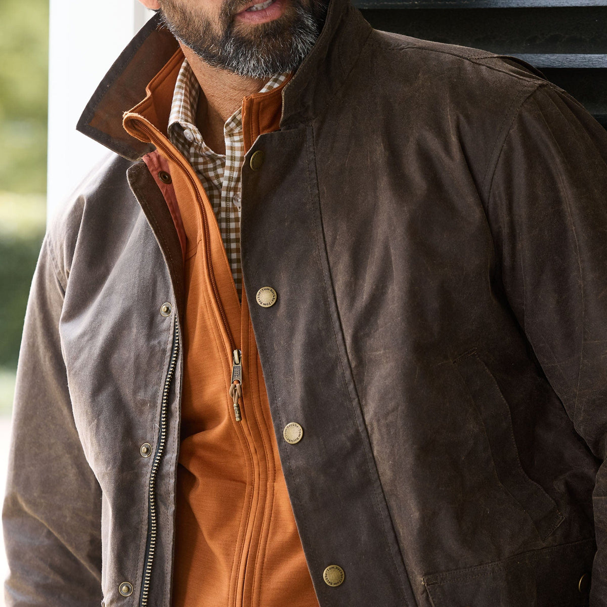 A man wears a brown waxed jacket over an orange zip-up and the Tom Beckbe Tucker Fleece Vest.