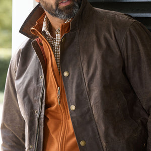 A man wears a brown waxed jacket over an orange zip-up and the Tom Beckbe Tucker Fleece Vest.