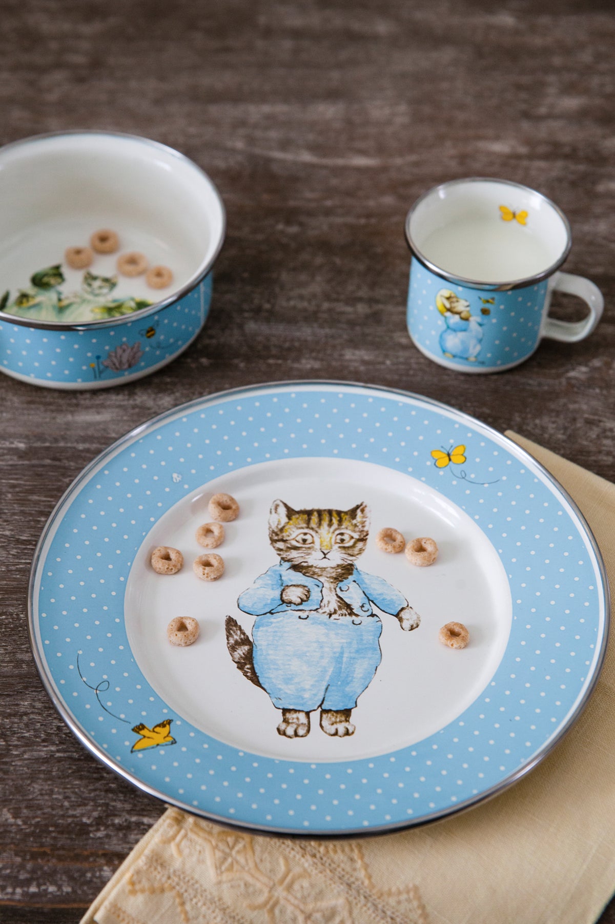 Close-up of Tom Kitten Child Set showcasing blue polka-dot enamelware and Tom Kitten illustration on a wooden table