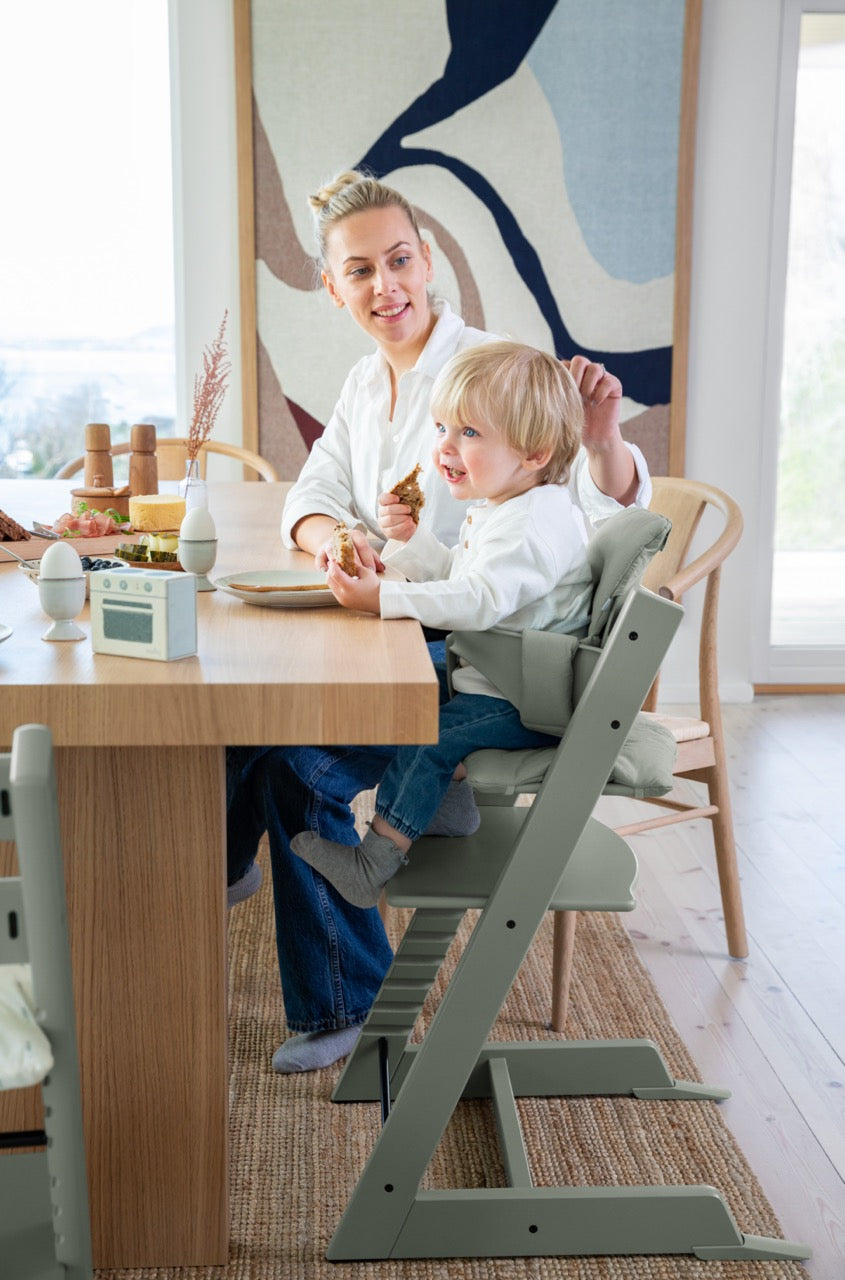 Toddler eating a snack in a Glacier Green Tripp Trapp High Chair² at a dining table with a smiling parent