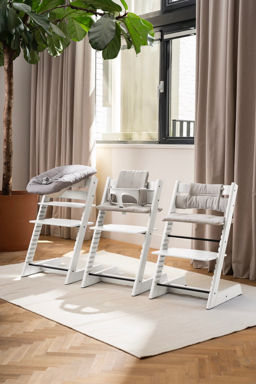 Front view of Tripp Trapp White high chair showing three configurations: newborn set, baby cushion, and adjustable footrest in a sunlit living room