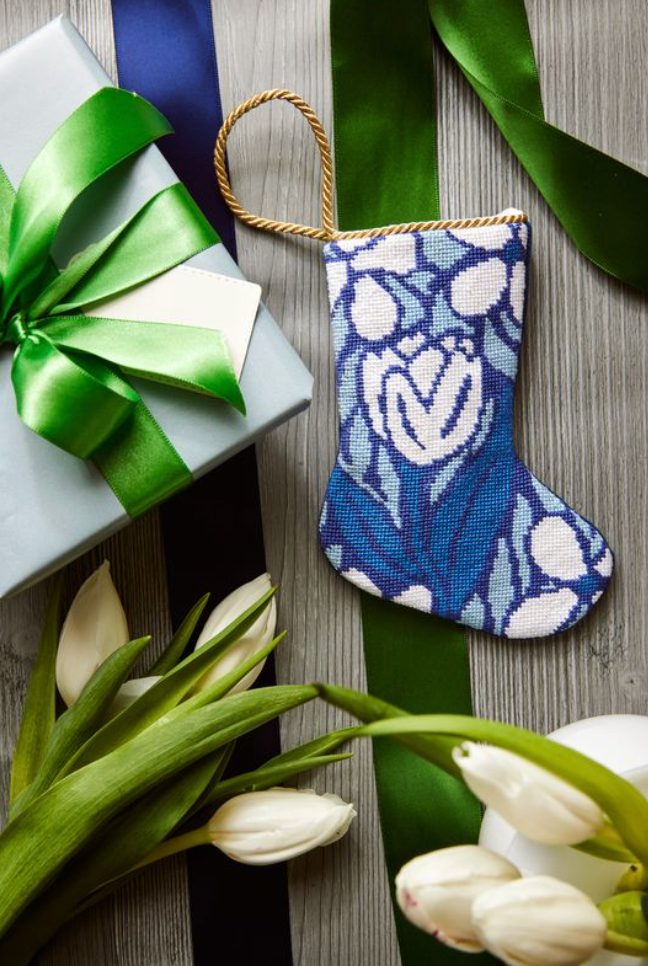 Front of Triumphant Tulip blue needlepoint stocking ornament with hand-stitched tulip motif and gold cord, styled with a gift and tulips