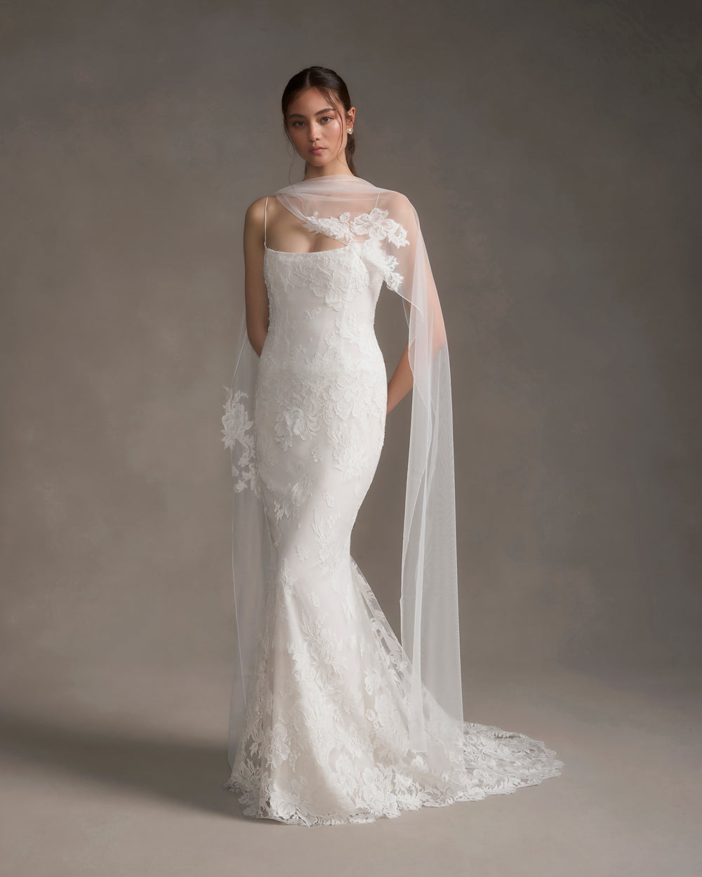 Front view of white tulle scarf with French lace clusters draped over model’s shoulders on neutral gray background