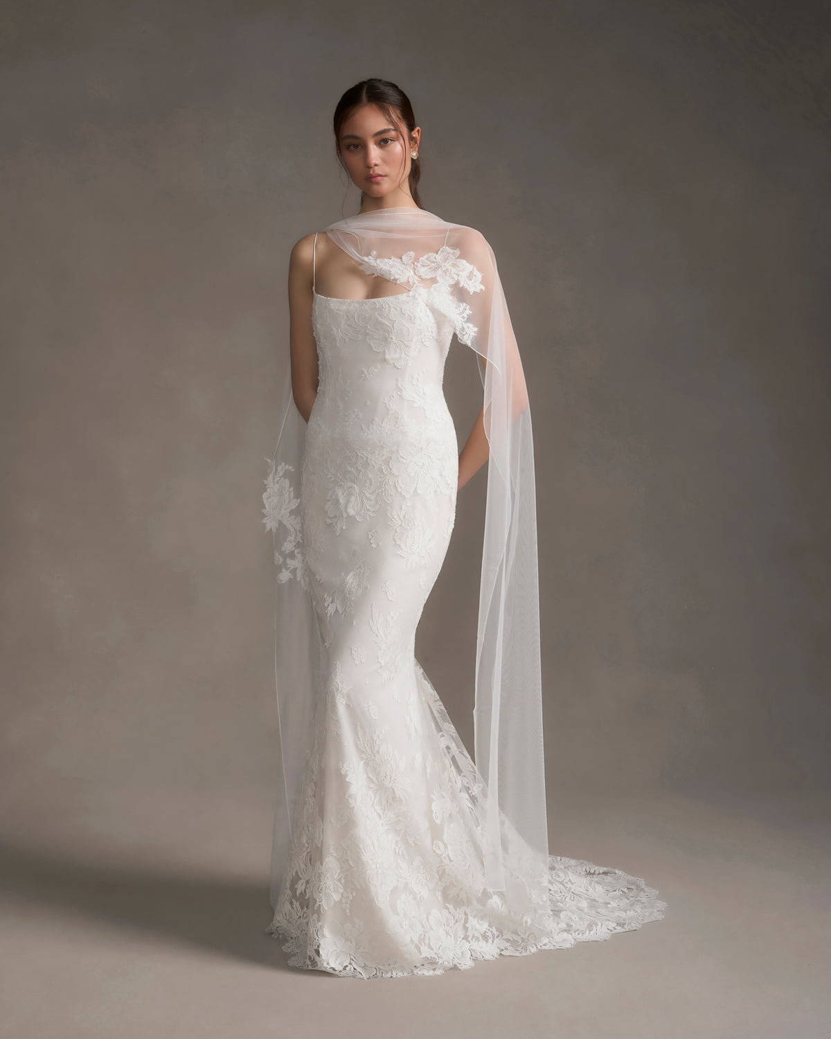 Front view of white tulle scarf with French lace clusters draped over model’s shoulders on neutral gray background