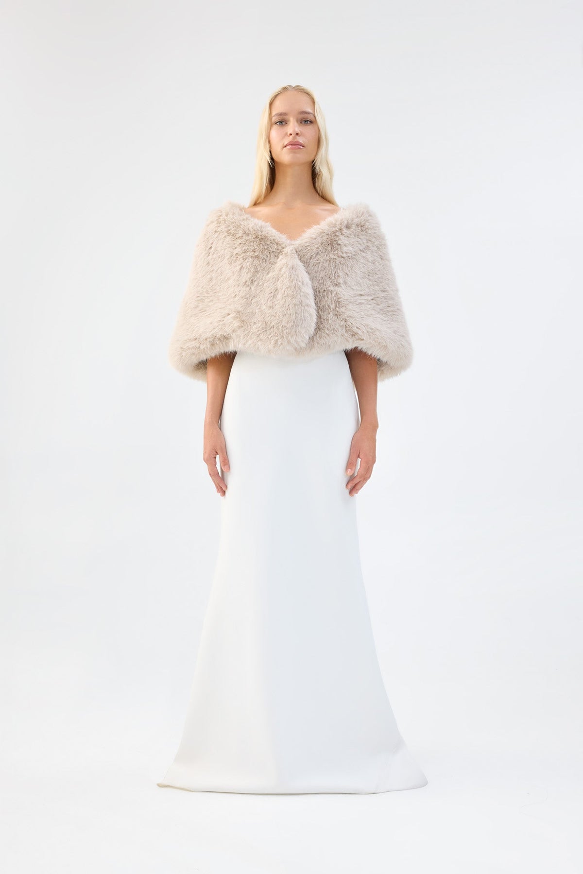 A model viewed from the front wearing a cream faux fur bridal wrap over a white gown.