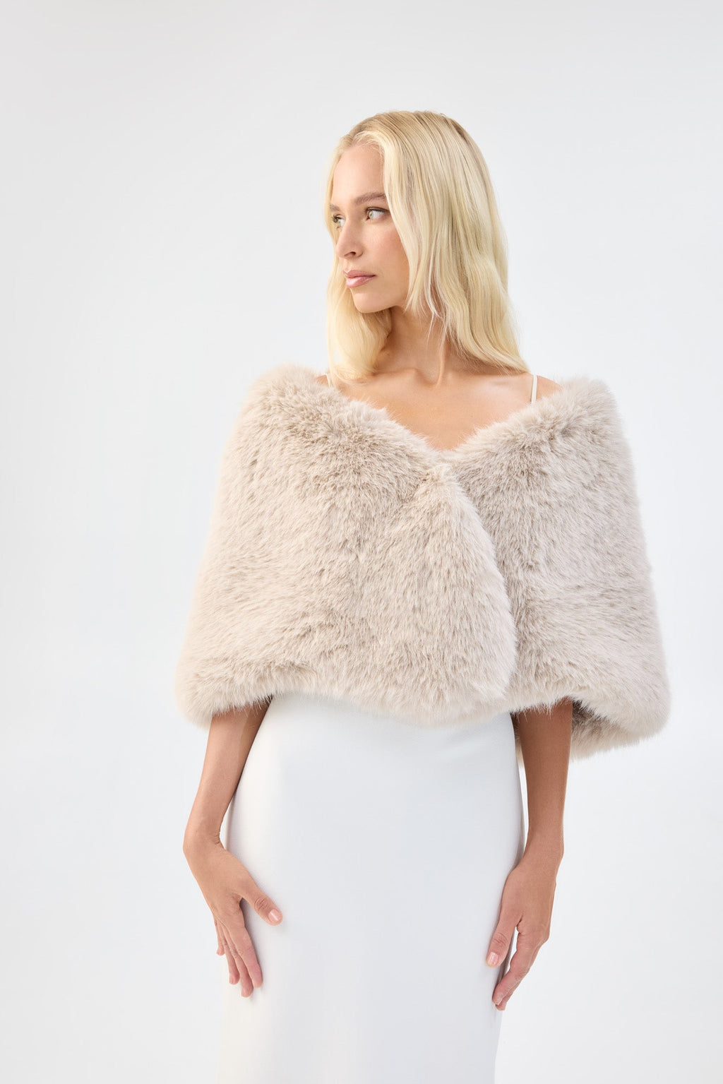 A model in three-quarter view wearing a cream faux fur bridal wrap over a white gown.