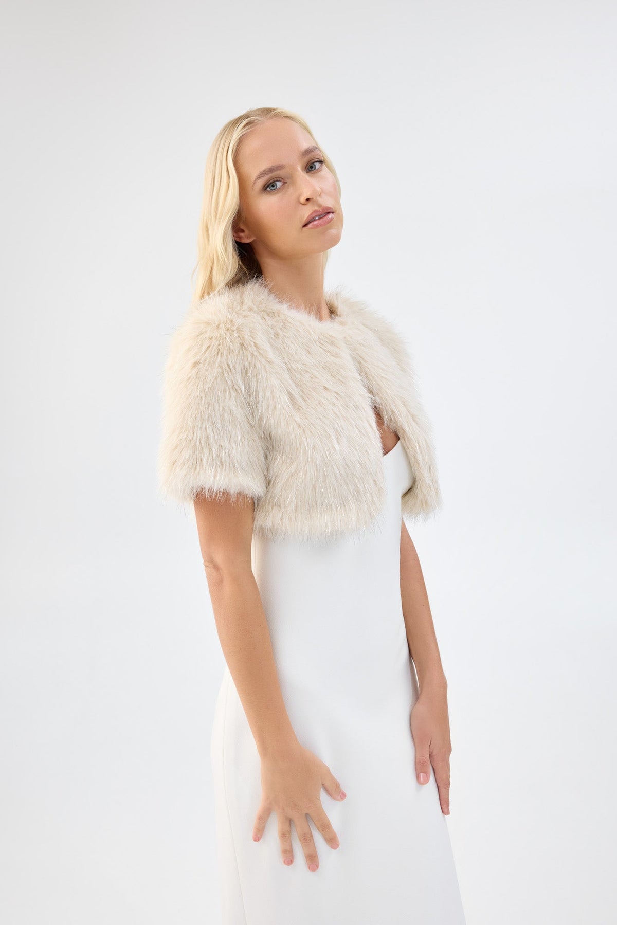 A model in three-quarter view wearing a metallic cream short-sleeve faux fur bridal bolero.