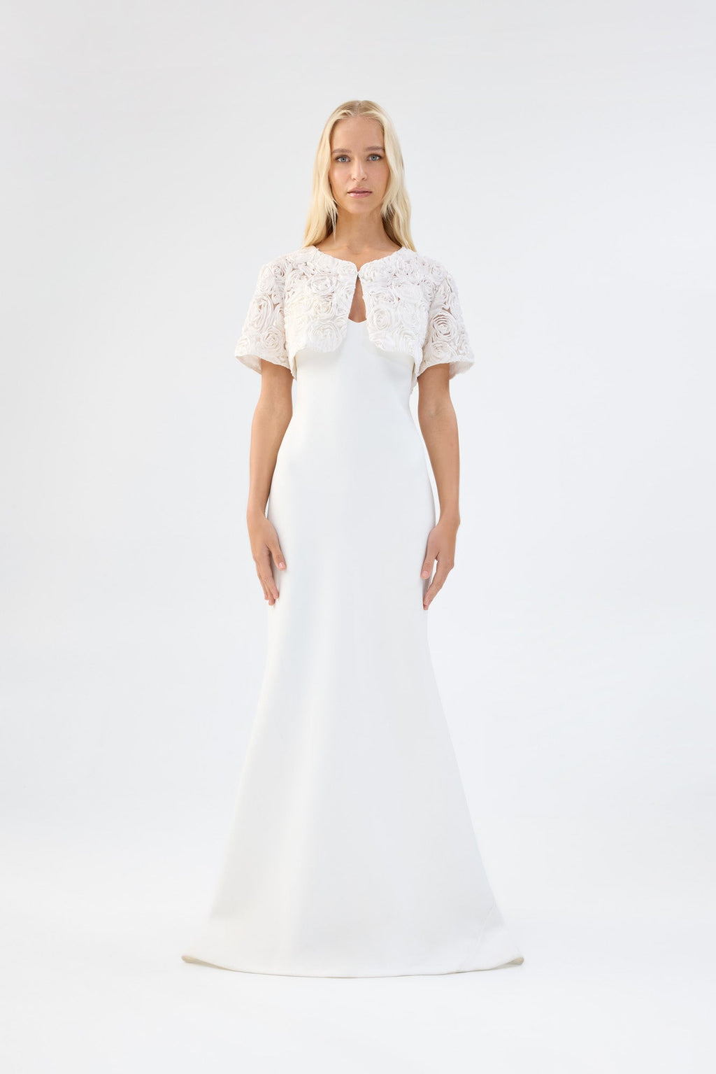 A model viewed from the front wearing a white floral textured bridal bolero over a white gown.