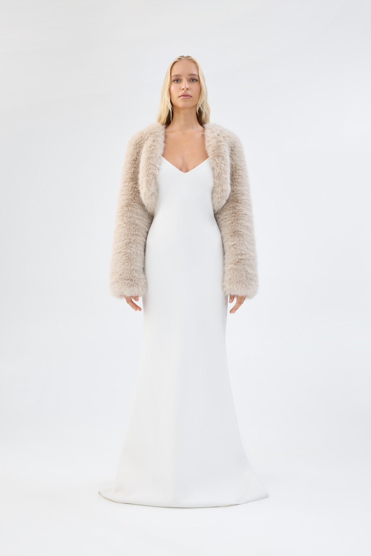 A model viewed from the front wearing a cream faux fur bridal cropped jacket over a white gown.