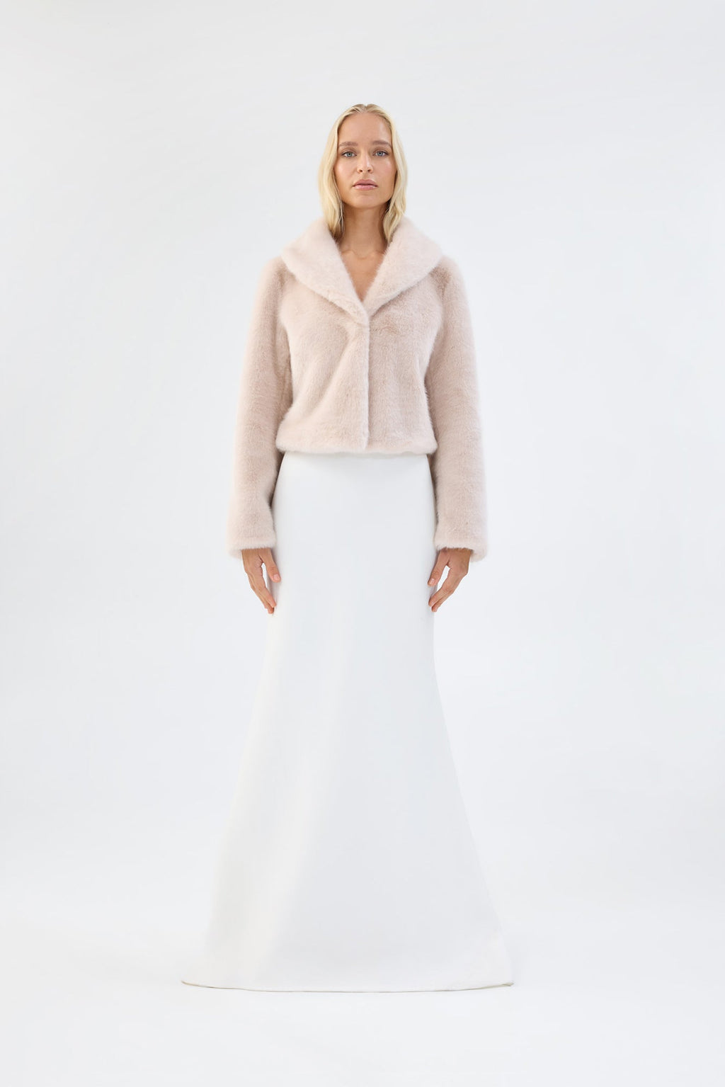 Blush pink faux fur jacket with notch lapel and cropped fit, worn over a white bridal dress