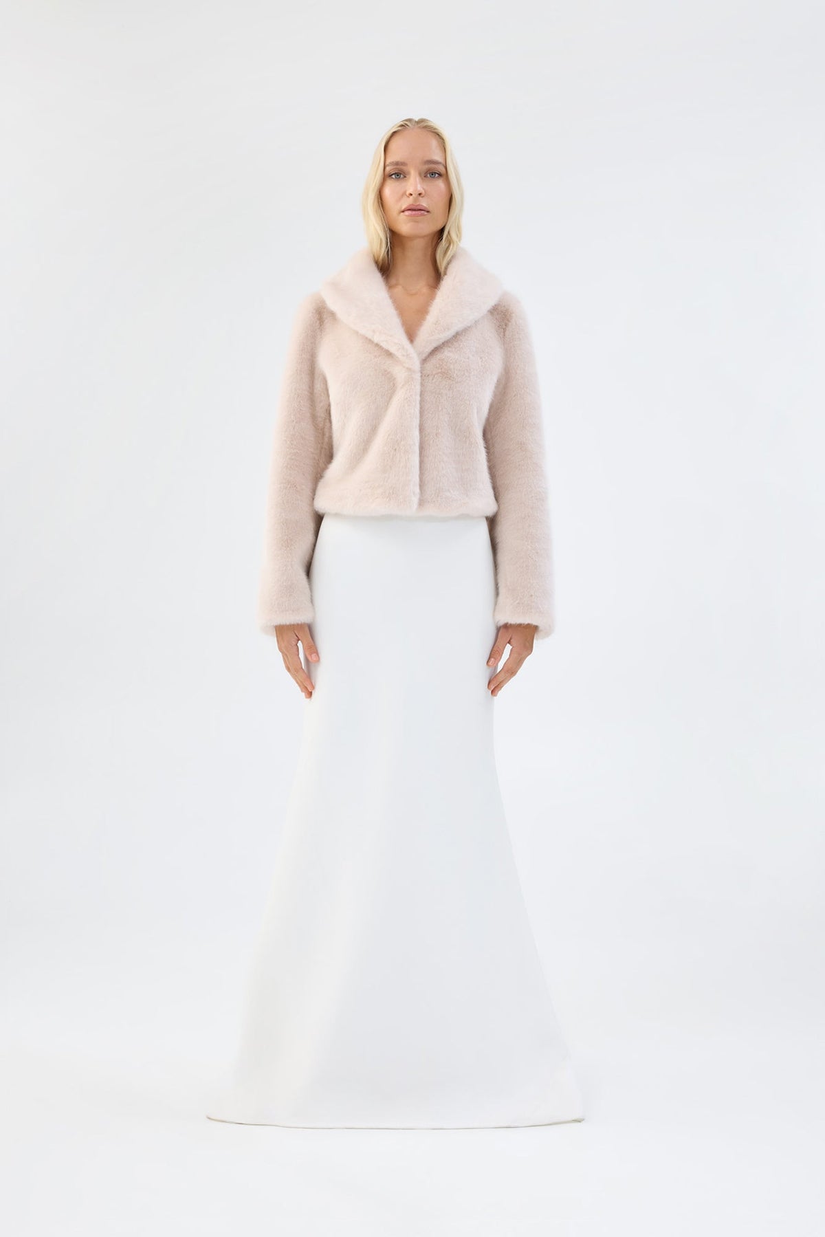 Blush pink faux fur jacket with notch lapel and cropped fit, worn over a white bridal dress