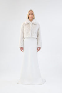 A model viewed from the front wearing a white cropped faux fur jacket over a white gown.