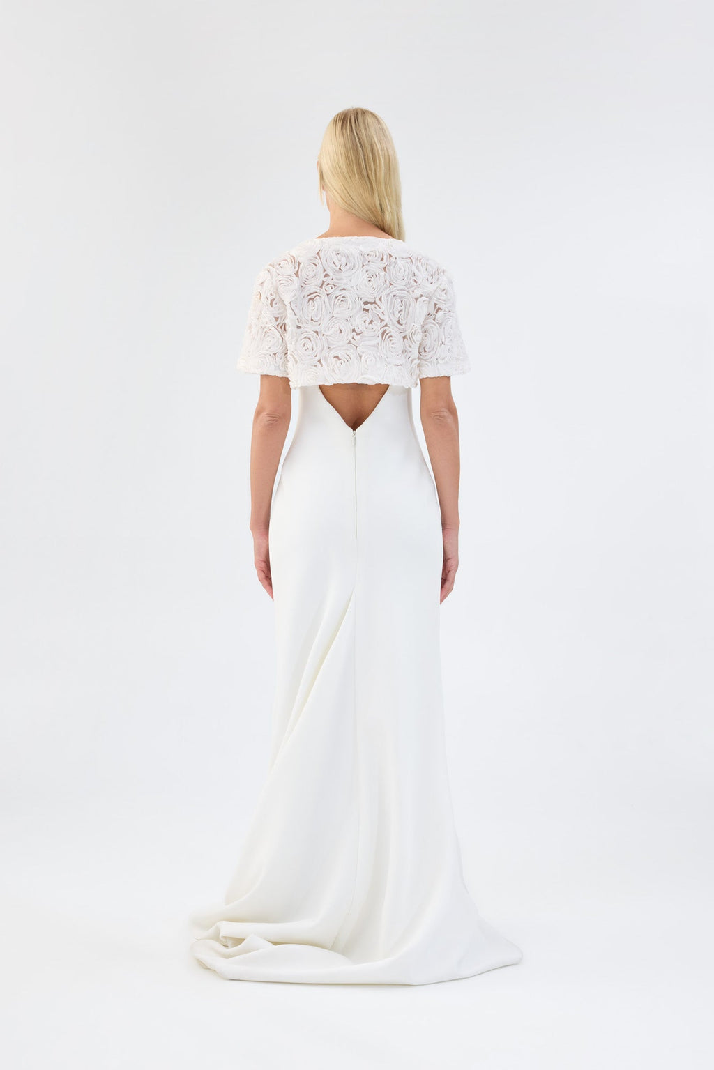 A model viewed from the back wearing a white floral textured bridal bolero over a white gown.