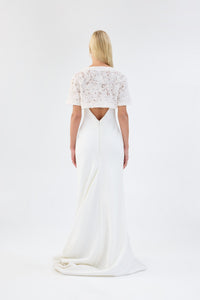 A model viewed from the back wearing a white floral textured bridal bolero over a white gown.