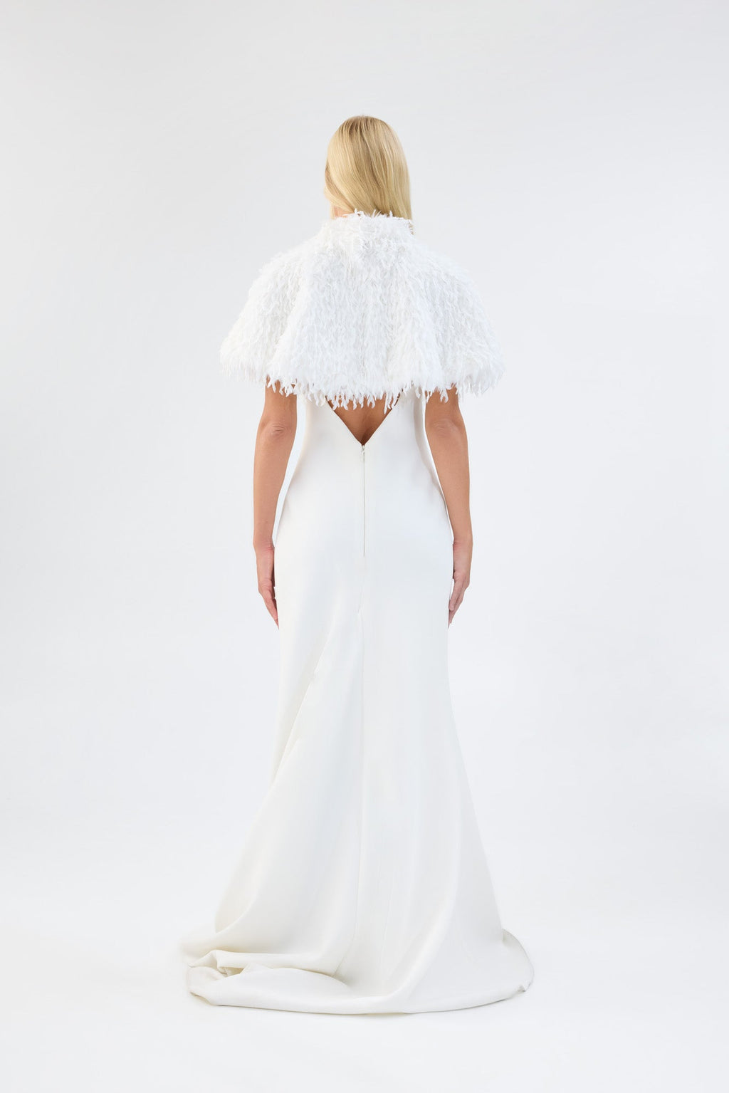 A model viewed from the back wearing a white textured faux fur bridal cape over a white gown.