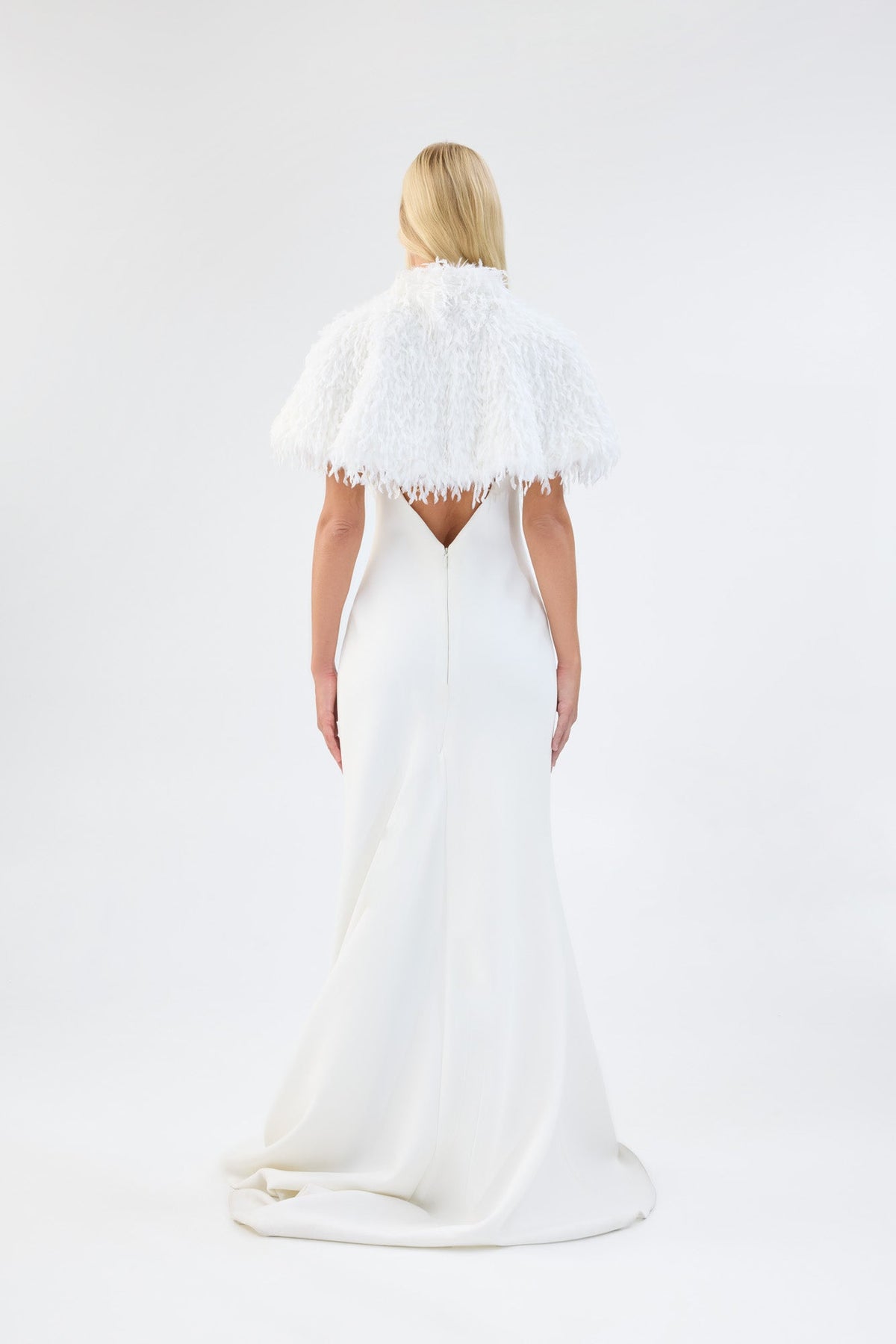 A model viewed from the back wearing a white textured faux fur bridal cape over a white gown.