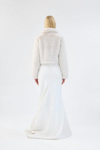 A model viewed from the back wearing a white cropped faux fur jacket over a white gown.