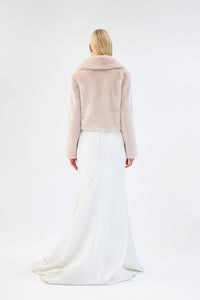 Back view of a blush pink faux fur jacket with notch lapel and cropped fit, worn over a white bridal dress
