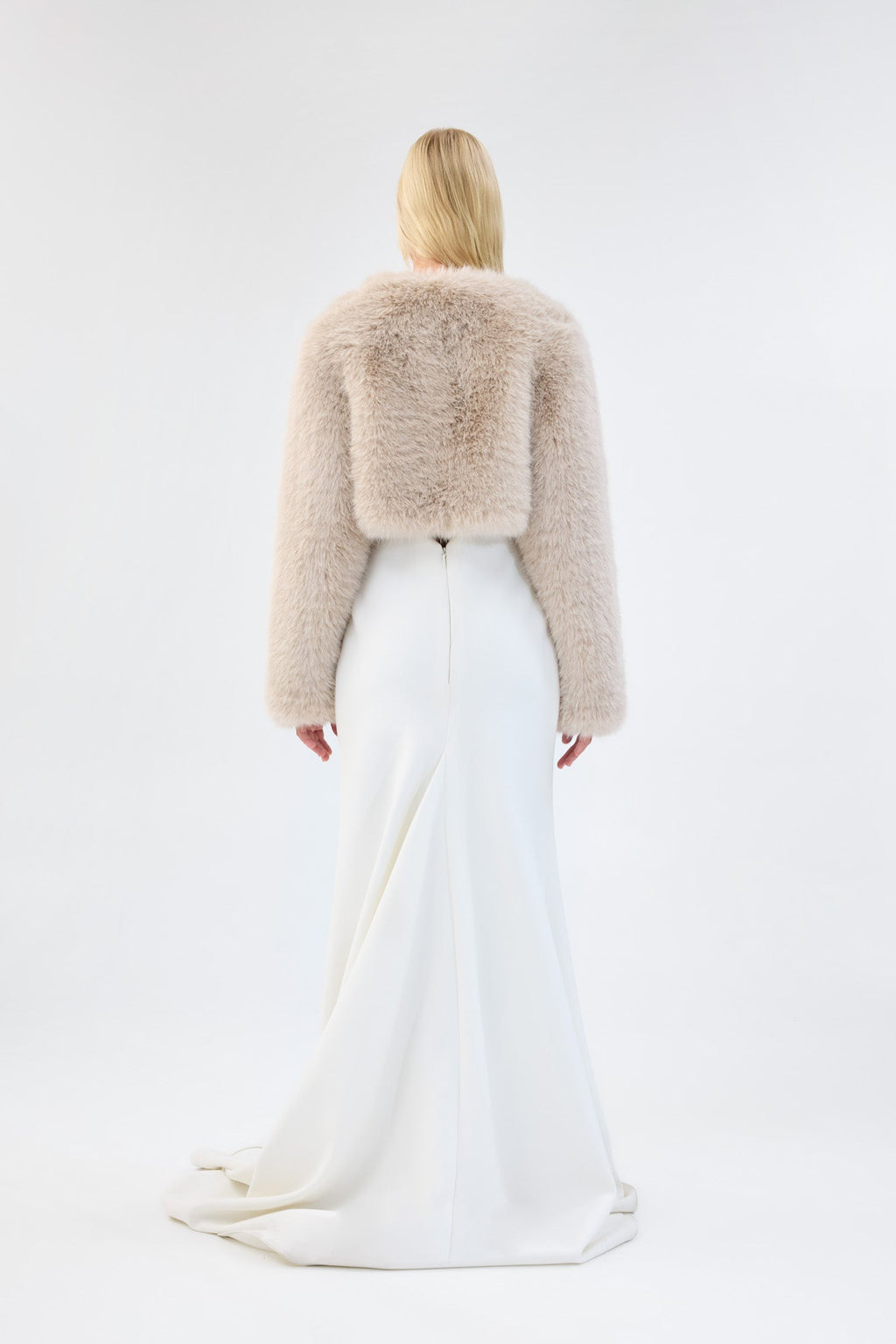 A model viewed from the front wearing a cream faux fur bridal cropped jacket over a white gown.