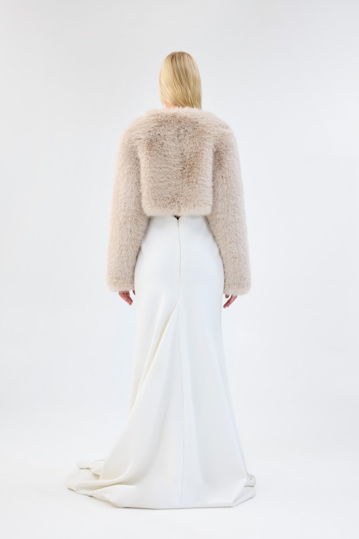 A model viewed from the front wearing a cream faux fur bridal cropped jacket over a white gown.