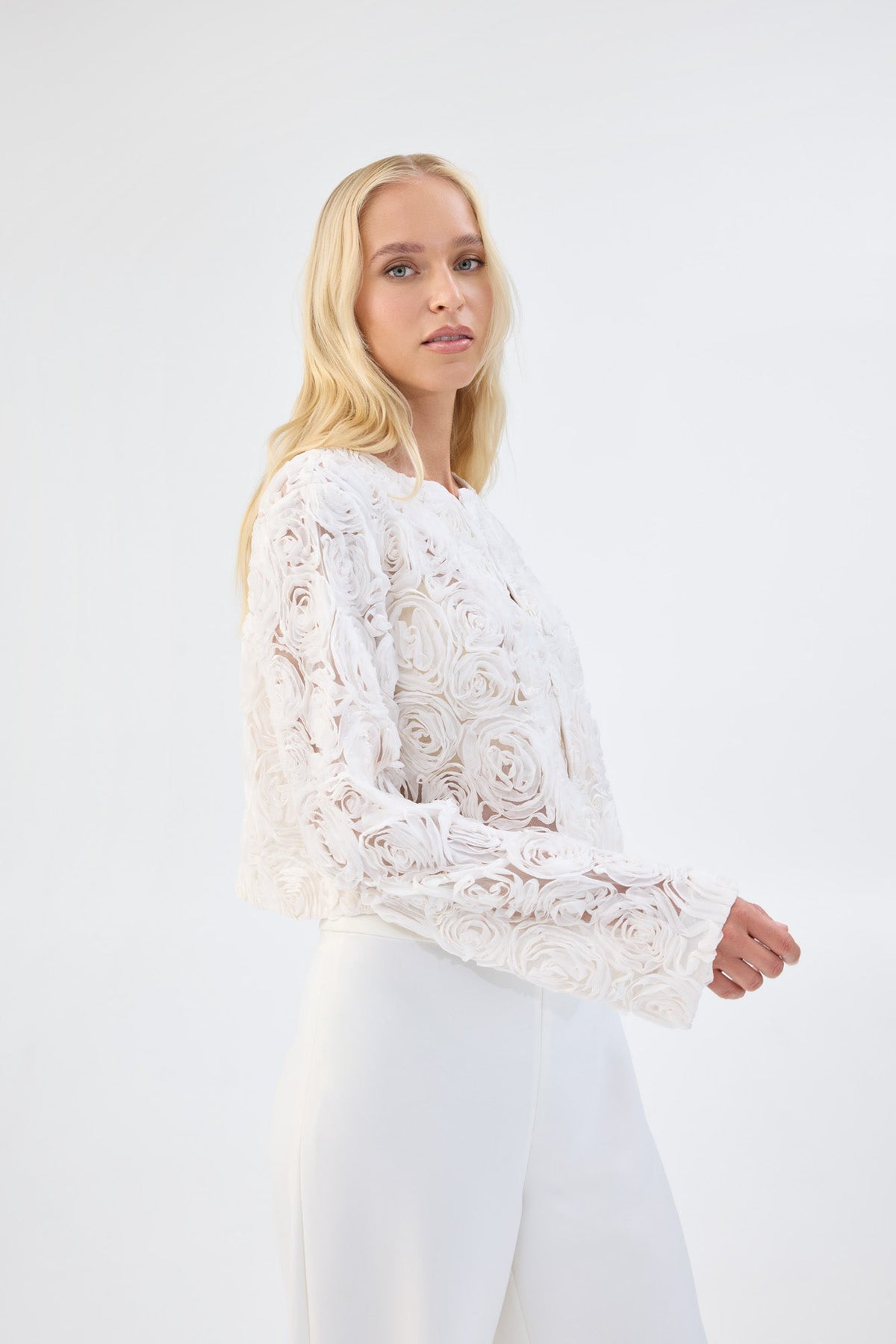 A model in side profile wearing a white floral textured cropped jacket.