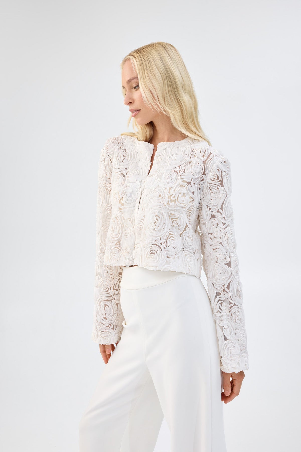 A model in three-quarter view wearing a white floral textured cropped jacket.