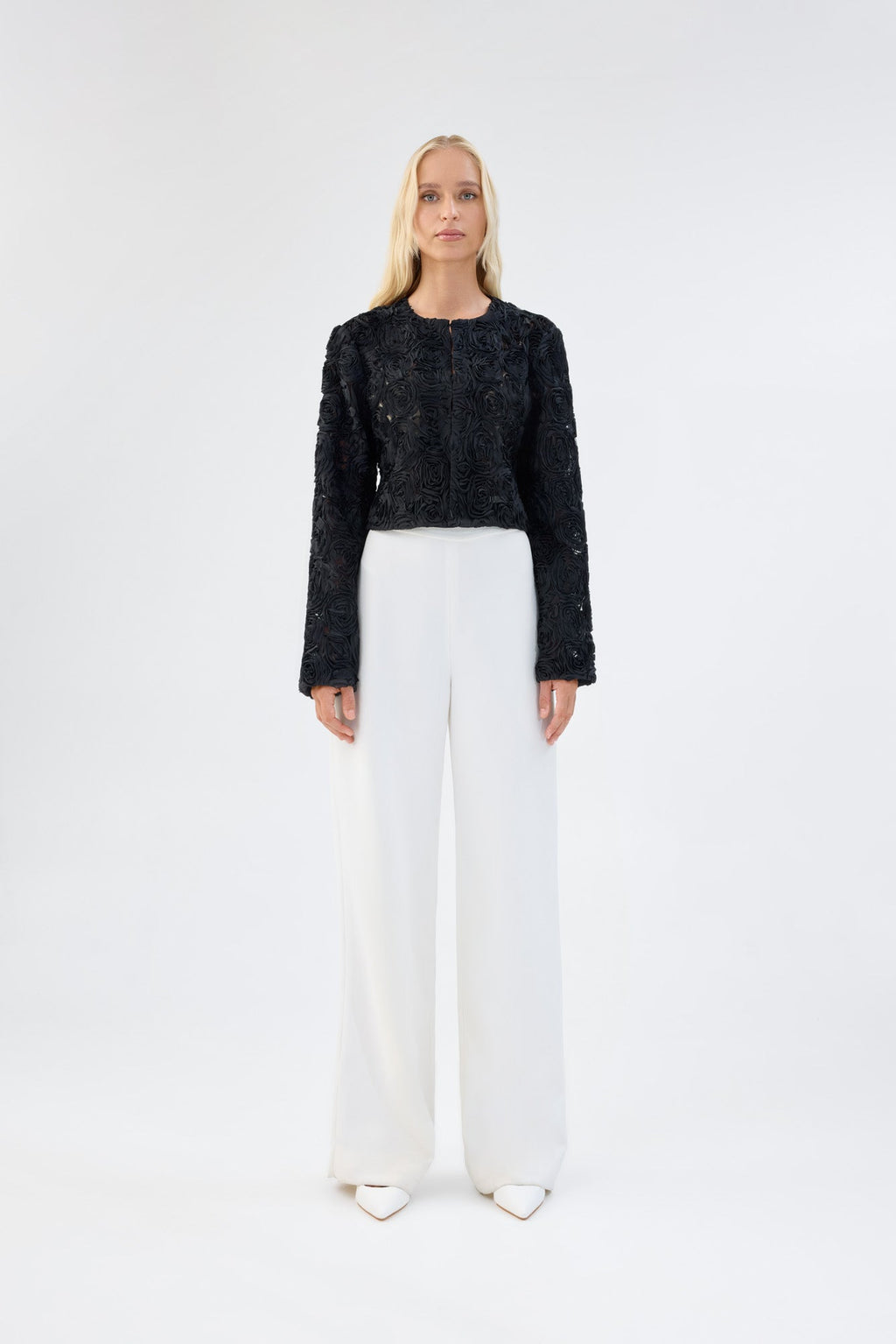 A model viewed from the front wearing a black floral textured cropped jacket.