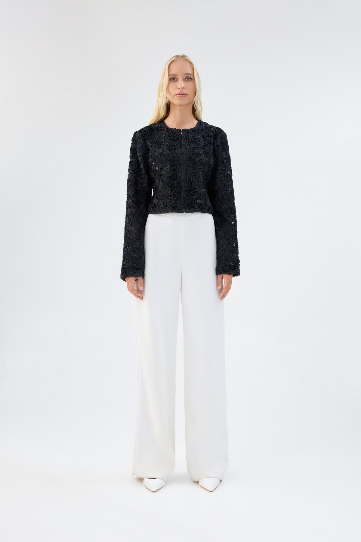 A model viewed from the front wearing a black floral textured cropped jacket.