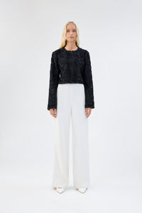 A model viewed from the front wearing a black floral textured cropped jacket.