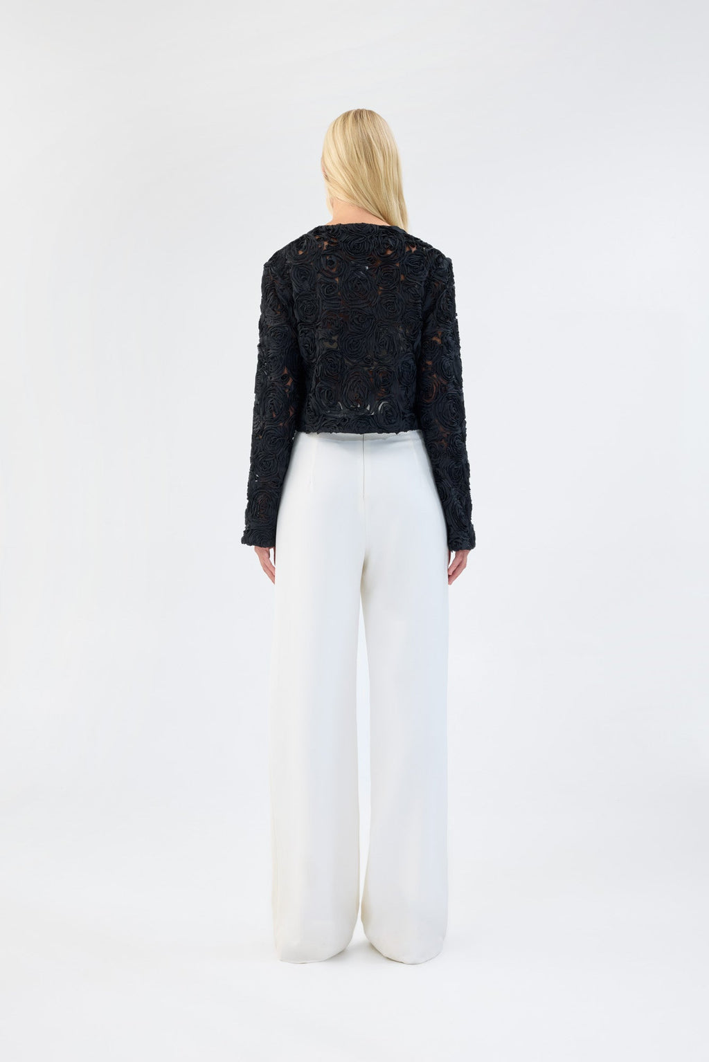 A model viewed from the back wearing a black floral textured cropped jacket.