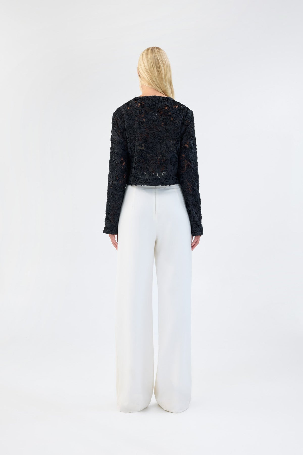 A model viewed from the back wearing a black floral textured cropped jacket.