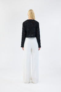 A model viewed from the back wearing a black floral textured cropped jacket.
