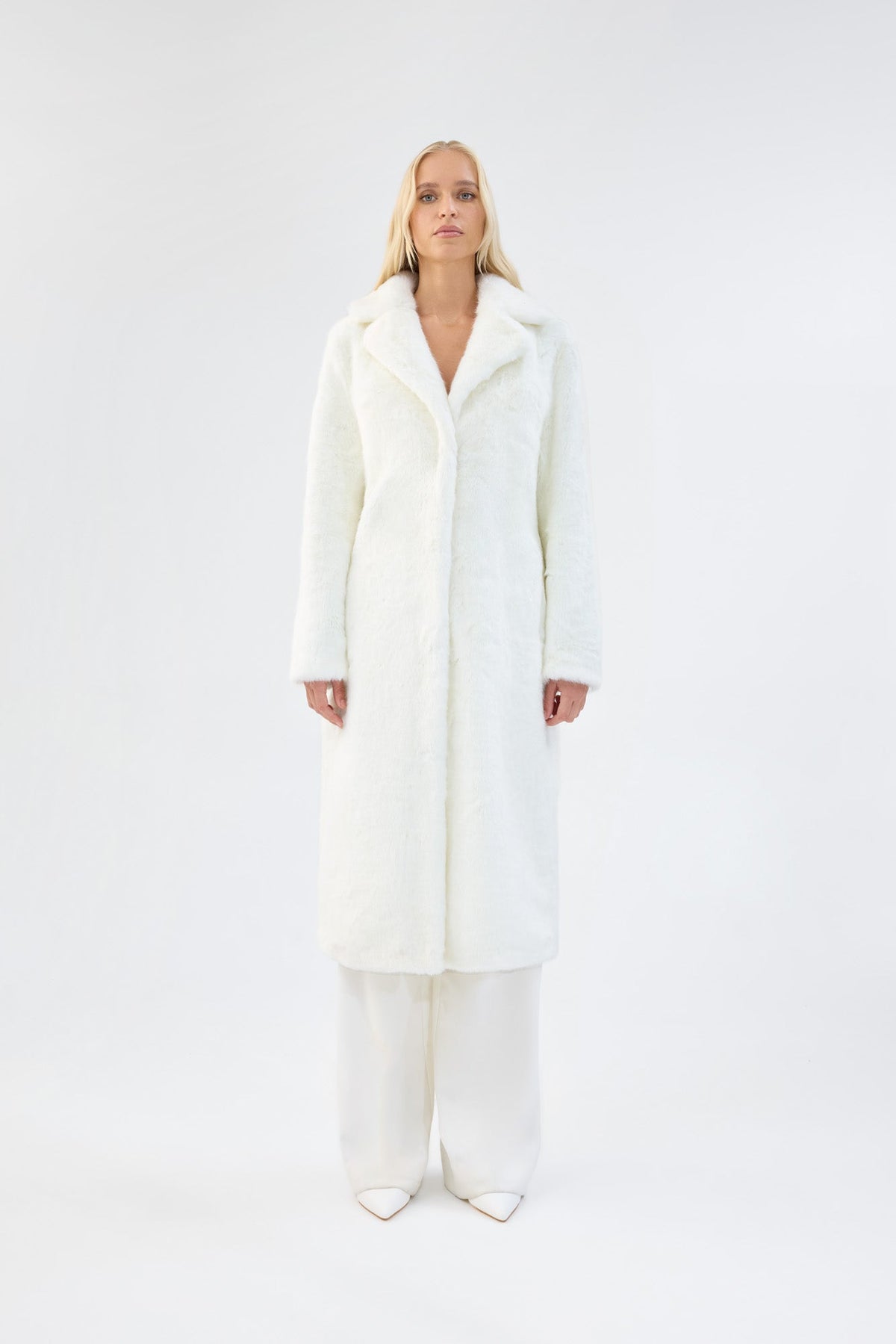 A model viewed from the front wearing a long white faux fur coat.