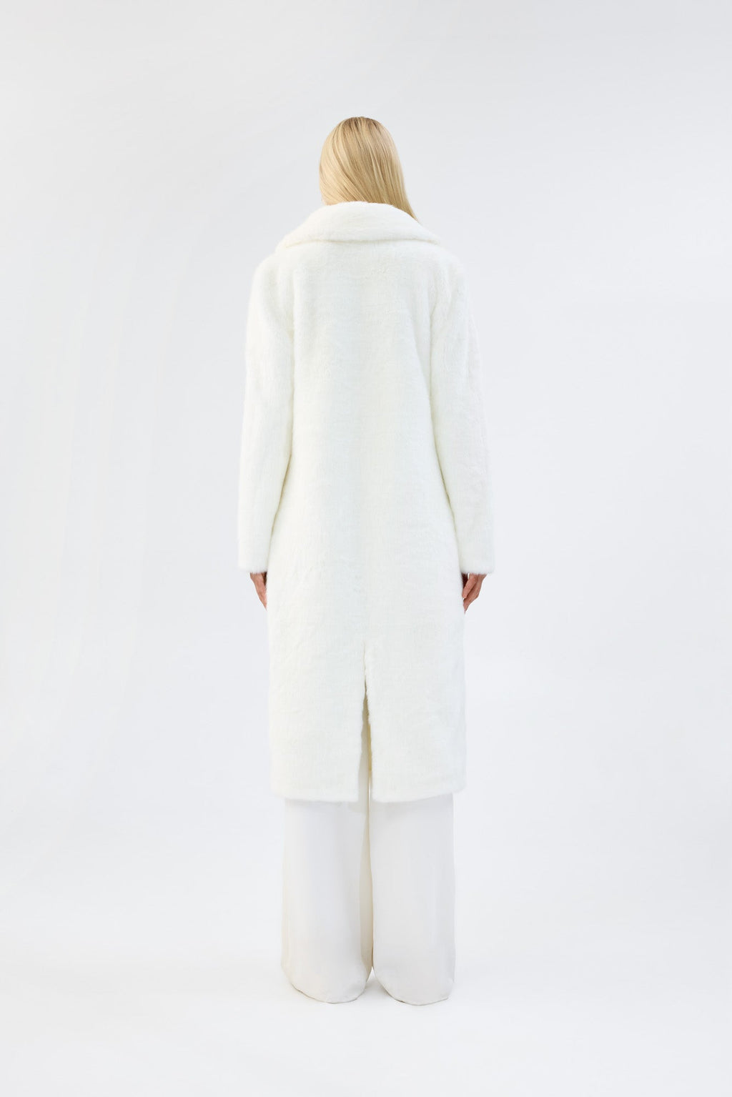A model viewed from the back wearing a long white faux fur coat.