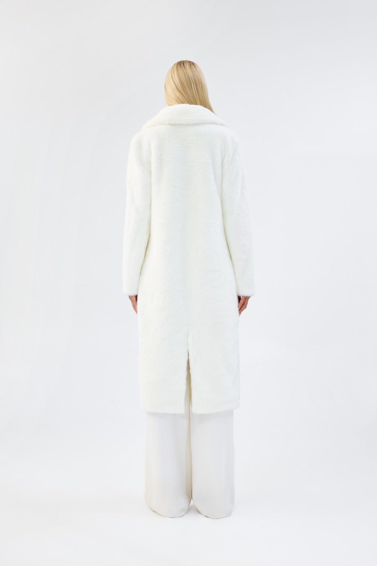 A model viewed from the back wearing a long white faux fur coat.