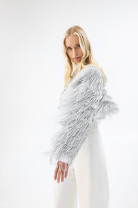 A model in three-quarter view wearing a cropped silver fringe jacket.