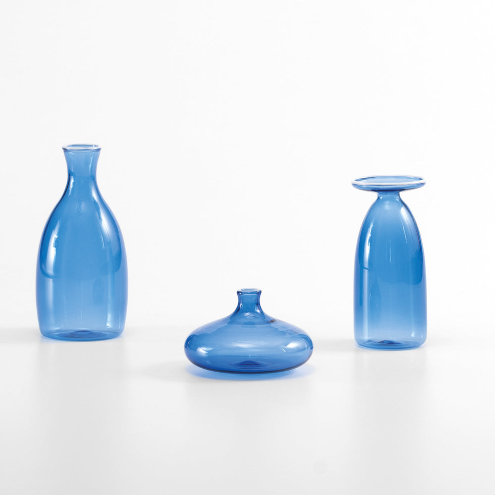 Front view of Un Fiore vases showcasing tall, low, and inverted silhouettes in light blue glass on white background
