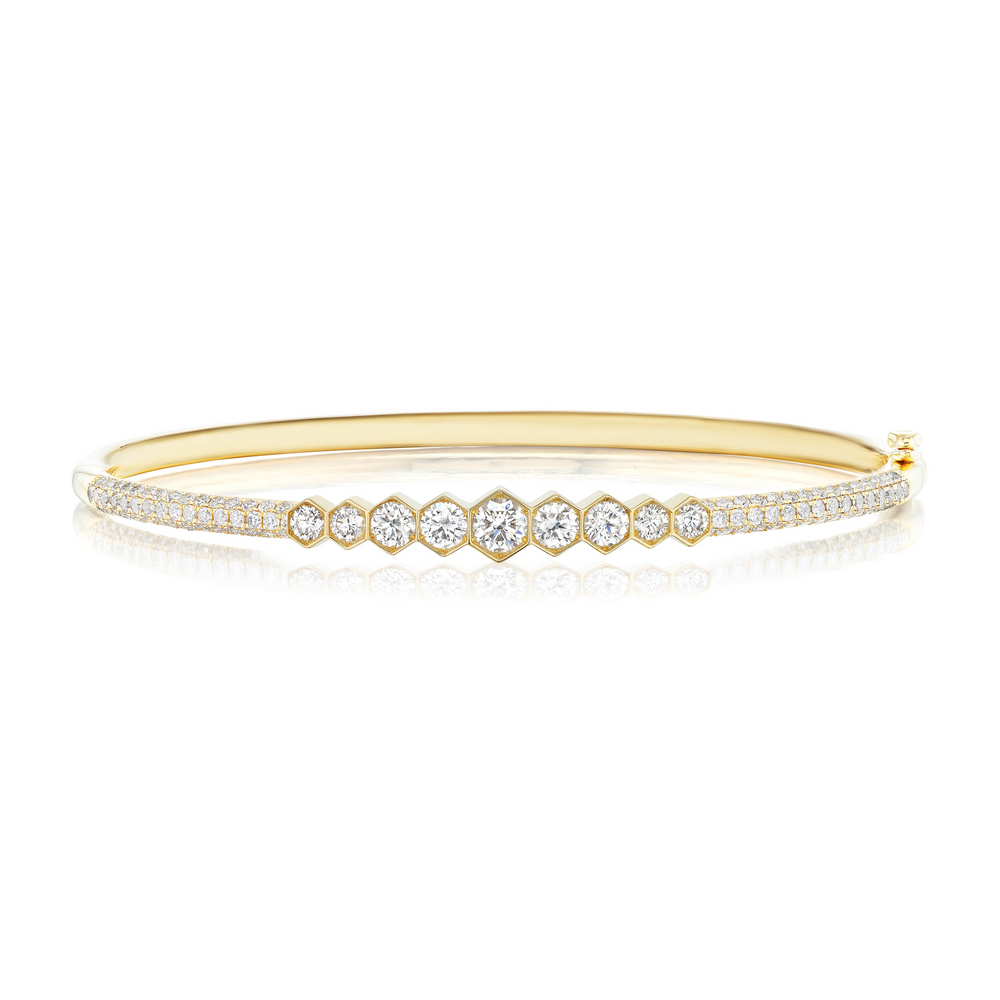 The Graduated Hexagon Bezel Set Diamond Pavé Bangle showcases a row of graduated SI clarity diamonds bezel set at the center, bordered by two pavé-set diamond rows on an elegant 18k gold band.