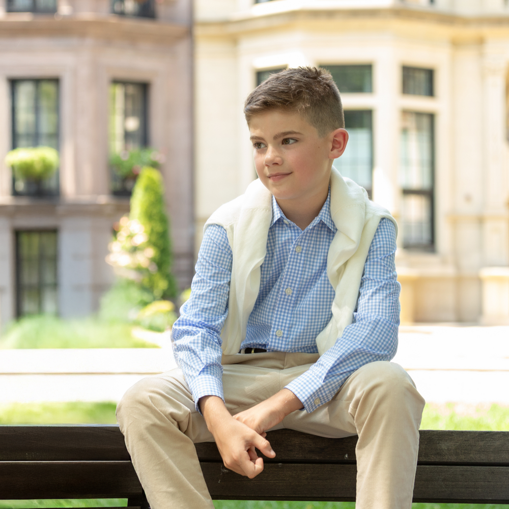 Seated boy wearing Bennett Button Down in Charles Street Check blue gingham, collar and sleeves visible, building background